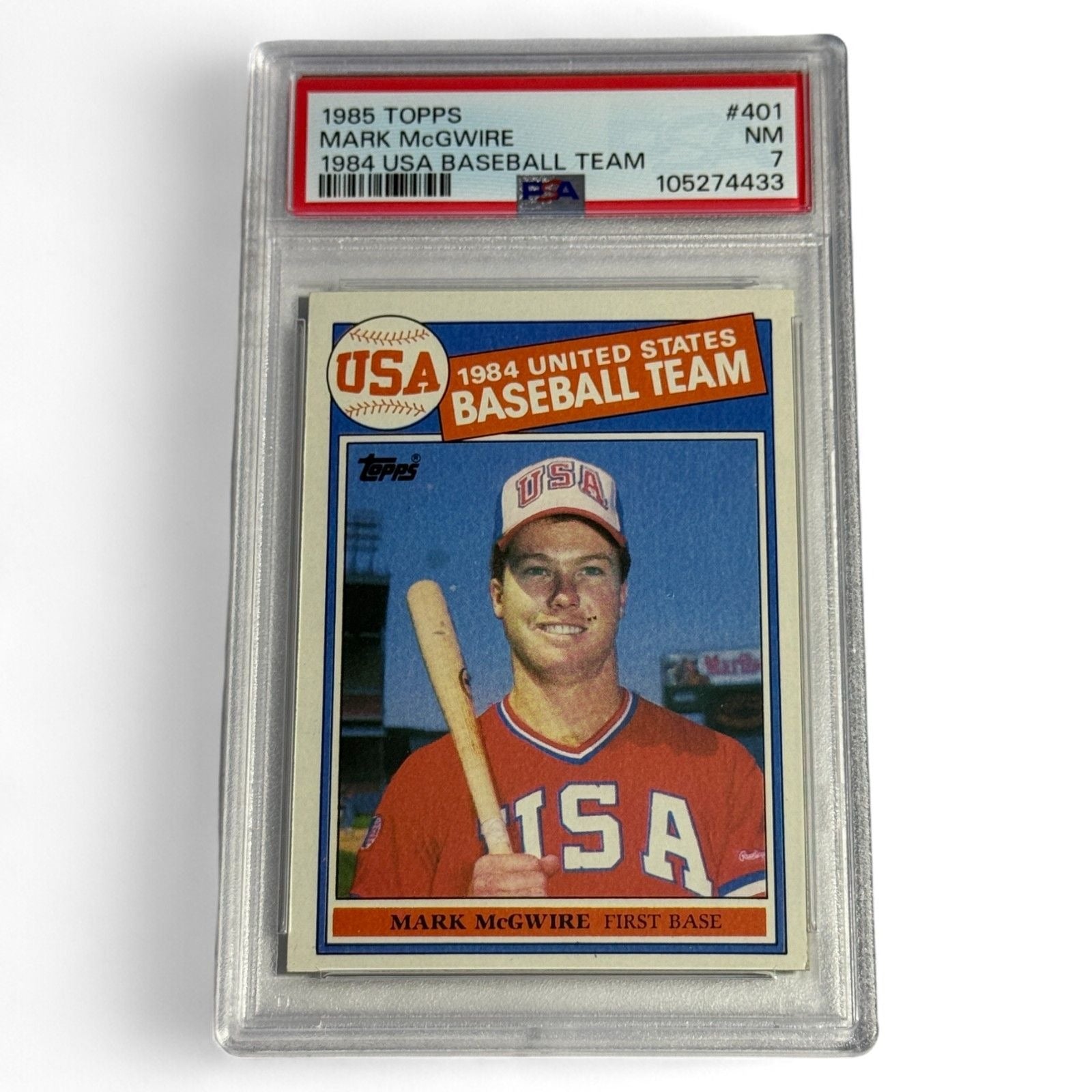 A PSA 7 near‑mint 1985 Topps #401 Mark McGwire rookie card featuring him in the 1984 USA Baseball Team uniform, an iconic Olympic‑era collectible.

