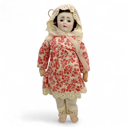 Antique porcelain doll in a floral red dress with lace trim and bonnet