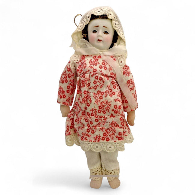 Antique porcelain doll in a floral red dress with lace trim and bonnet