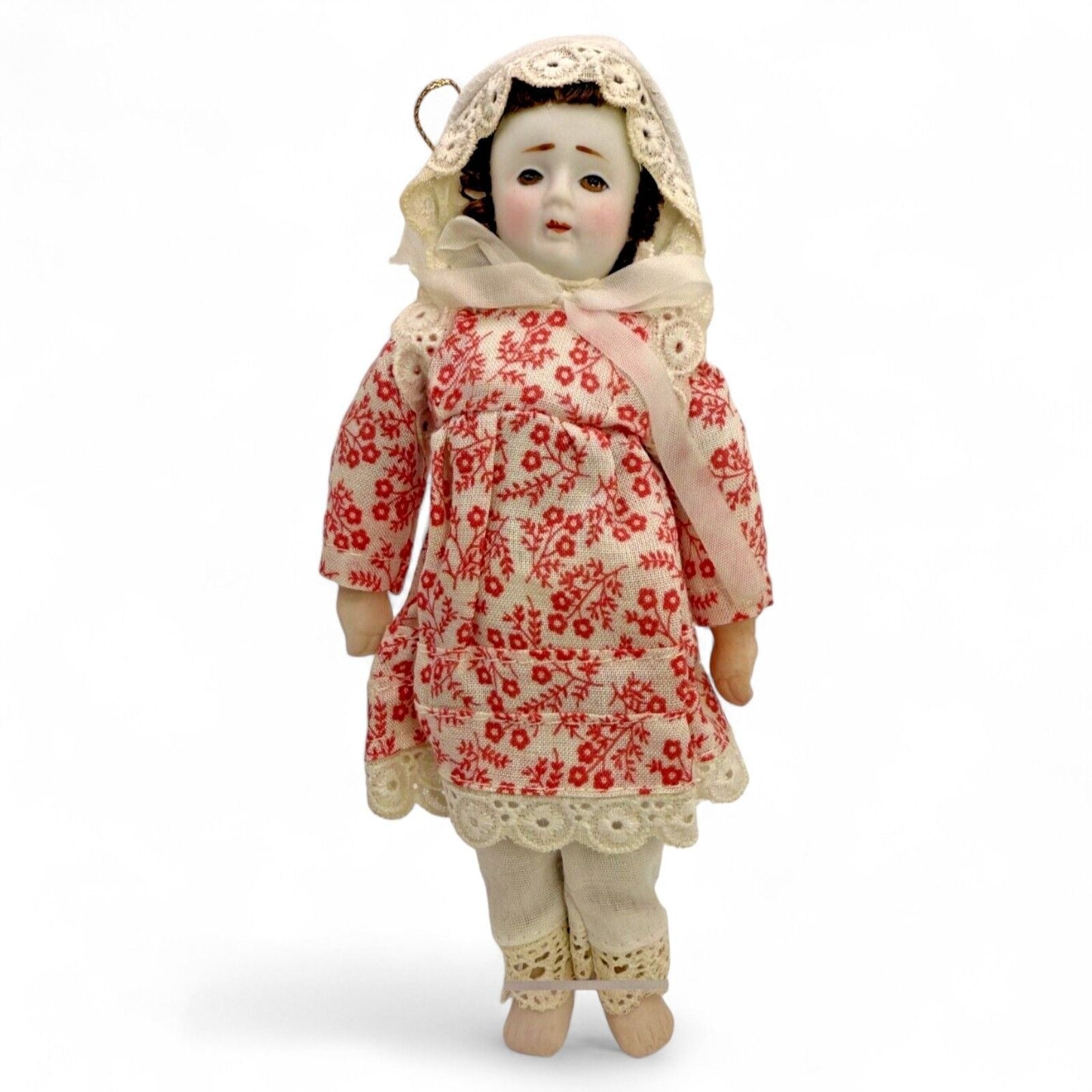 Antique porcelain doll in a floral red dress with lace trim and bonnet
