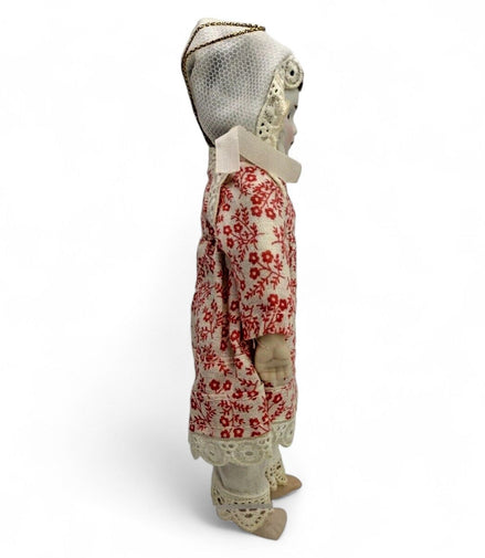 Side view of a vintage porcelain doll in a red floral dress with lace details