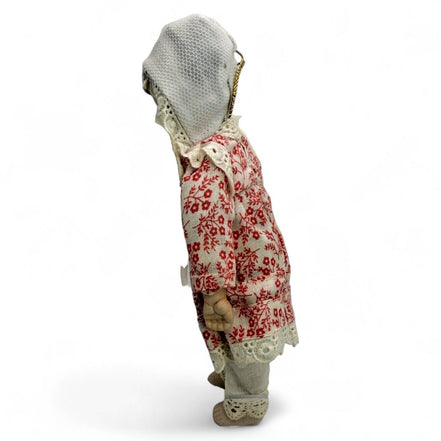 Side profile of an antique doll in a red floral dress with lace bonnet