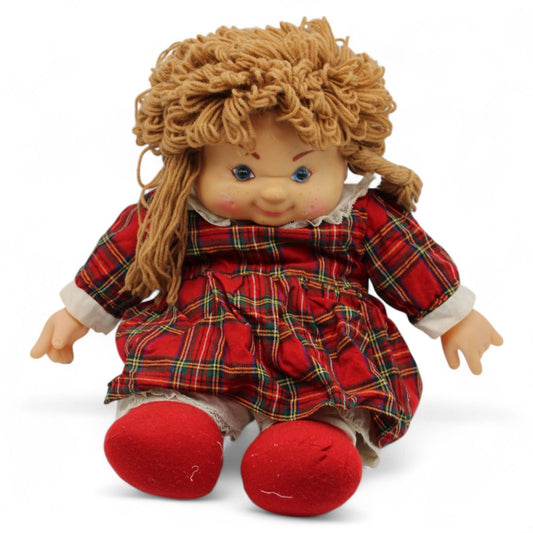 A vintage Heather Christmas doll by Scottish House of Lloyd featuring a vinyl face, yarn hair, and dressed in a festive tartan dress with red booties.
