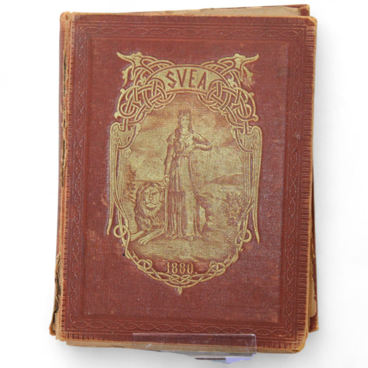Front cover of Svea Folk-Kalender 1880 showing embossed red cloth with golden illustration of woman and lion.  
