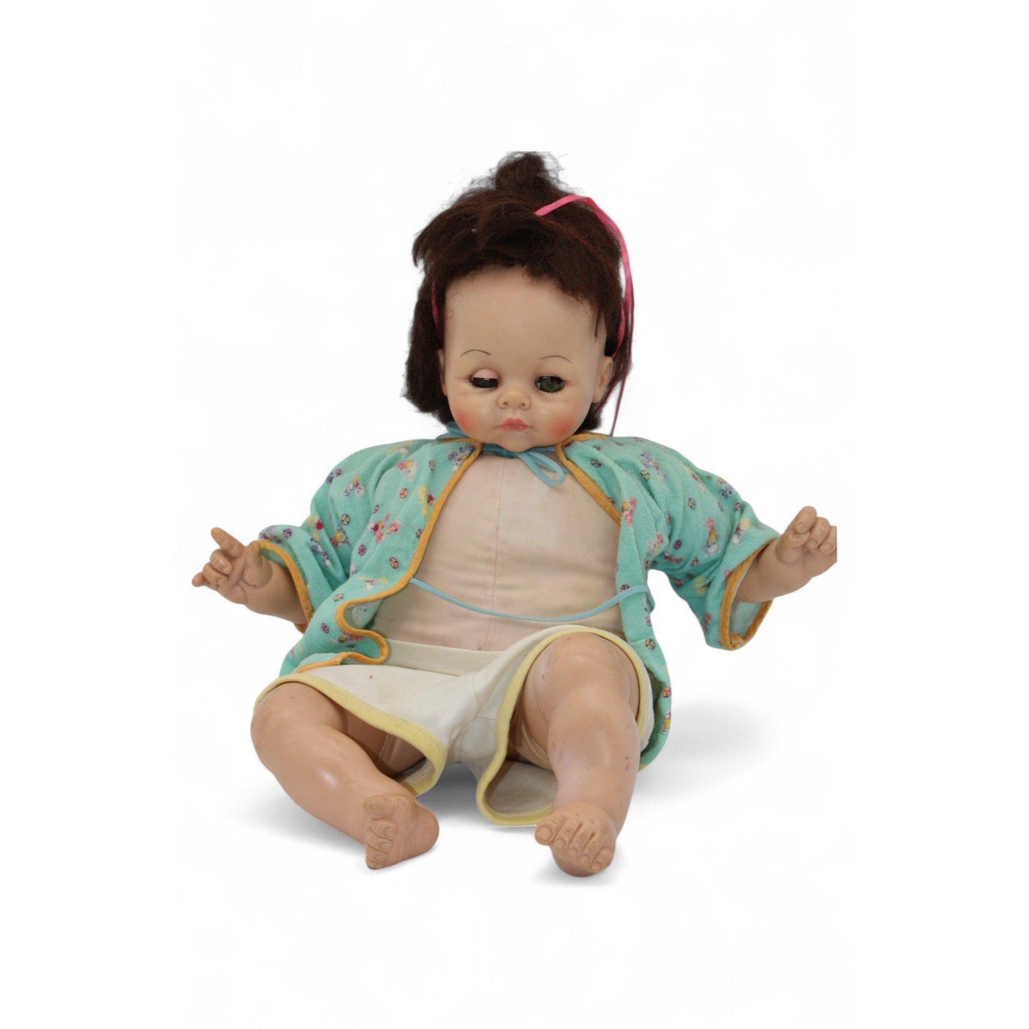 Vintage baby doll wearing a green floral jacket with yellow trim, featuring brown hair and glass eyes.