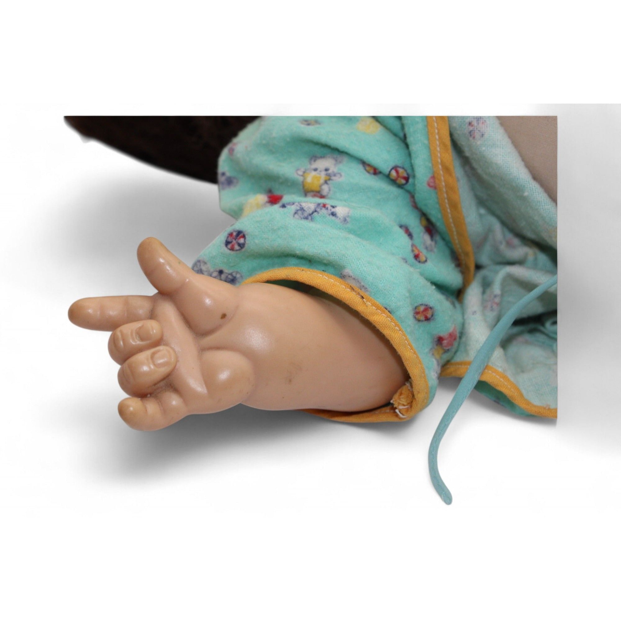 Vintage baby doll wearing a green floral jacket with yellow trim, featuring brown hair and glass eyes.
