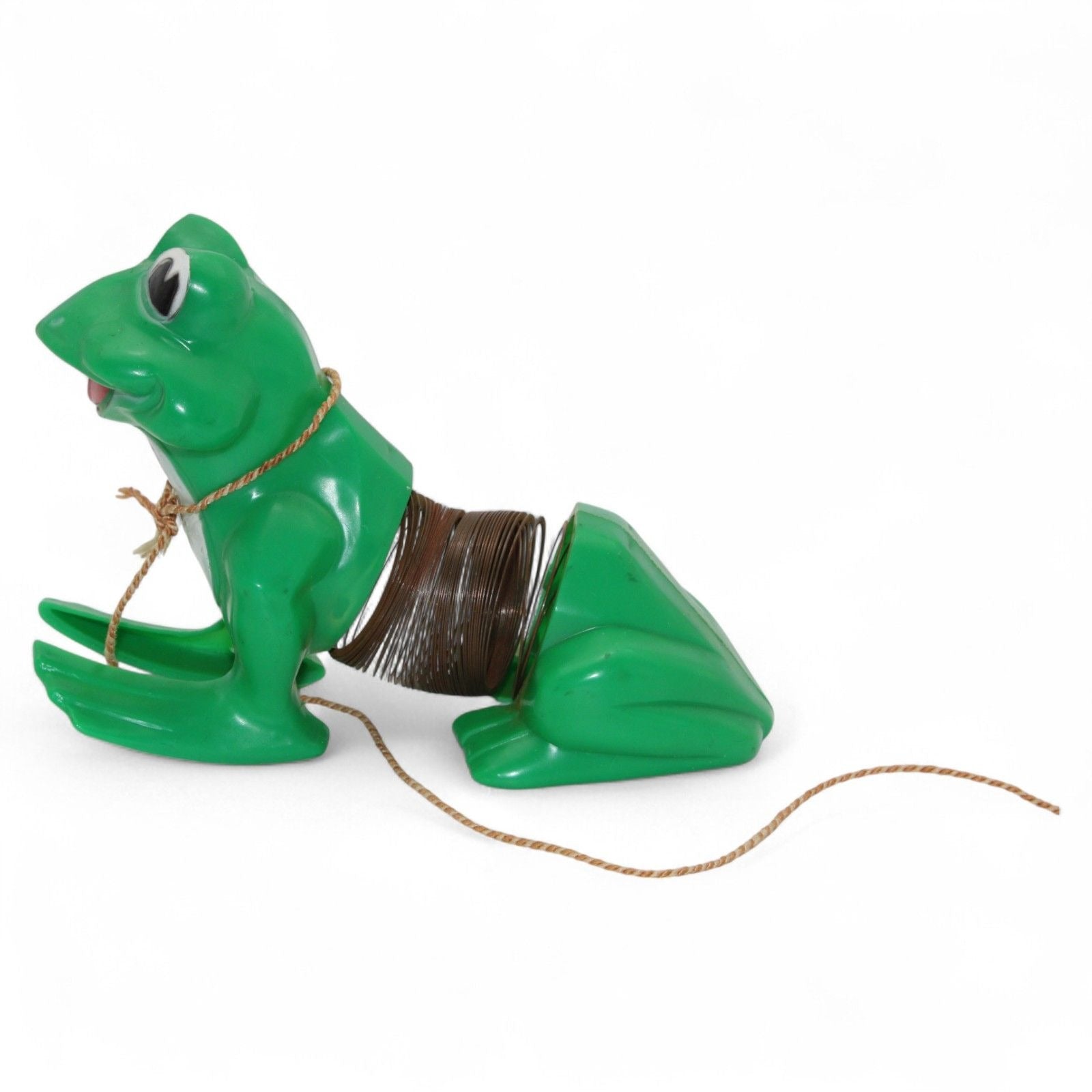 Vintage green plastic frog with pull-along rope and built-in cassette/spool tape mechanism. Frog wears a painted tuxedo bib and has a red smiling mouth. Pull the cord to wind the internal tape wheel and release it to watch the frog's "belly" spool slowly unwind, likely playing a jingling or recorded sound. Charming retro mechanical toy — a whimsical novelty from days gone by!
