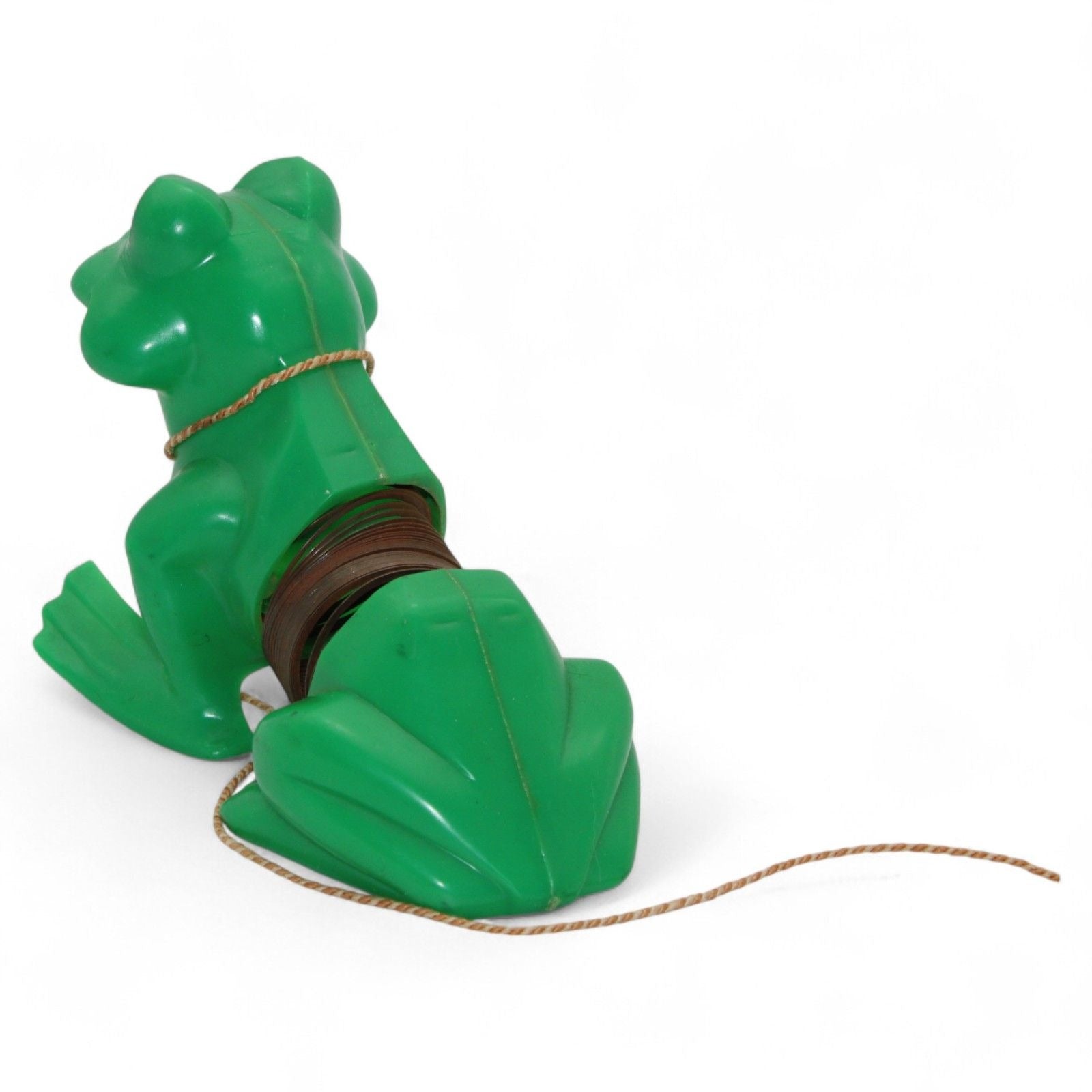 Vintage green plastic frog with pull-along rope and built-in cassette/spool tape mechanism. Frog wears a painted tuxedo bib and has a red smiling mouth. Pull the cord to wind the internal tape wheel and release it to watch the frog's "belly" spool slowly unwind, likely playing a jingling or recorded sound. Charming retro mechanical toy — a whimsical novelty from days gone by!
