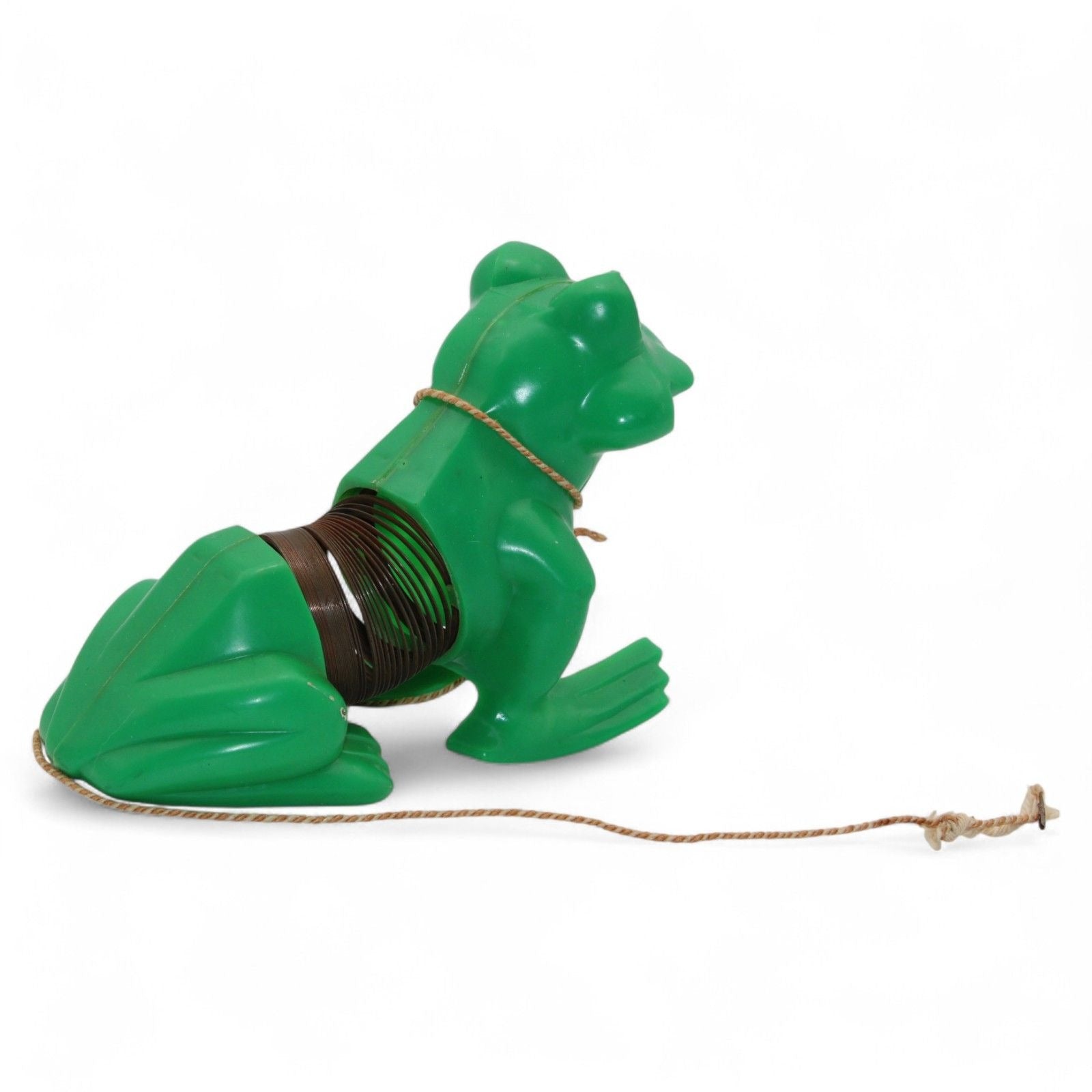 Vintage green plastic frog with pull-along rope and built-in cassette/spool tape mechanism. Frog wears a painted tuxedo bib and has a red smiling mouth. Pull the cord to wind the internal tape wheel and release it to watch the frog's "belly" spool slowly unwind, likely playing a jingling or recorded sound. Charming retro mechanical toy — a whimsical novelty from days gone by!
