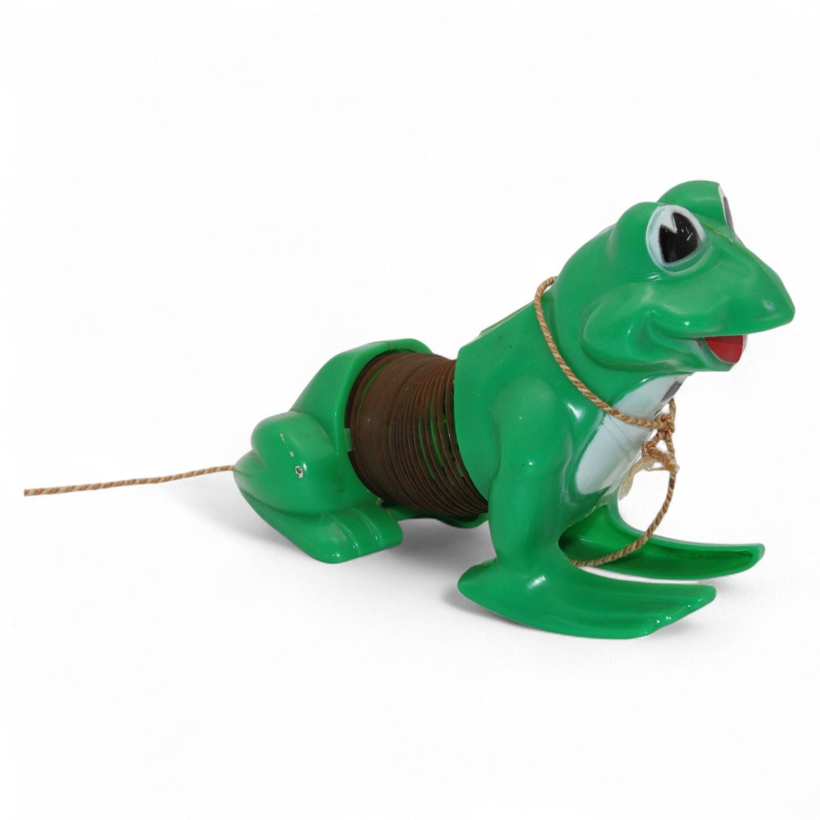 Vintage green plastic frog with pull-along rope and built-in cassette/spool tape mechanism. Frog wears a painted tuxedo bib and has a red smiling mouth. Pull the cord to wind the internal tape wheel and release it to watch the frog's "belly" spool slowly unwind, likely playing a jingling or recorded sound. Charming retro mechanical toy — a whimsical novelty from days gone by!
