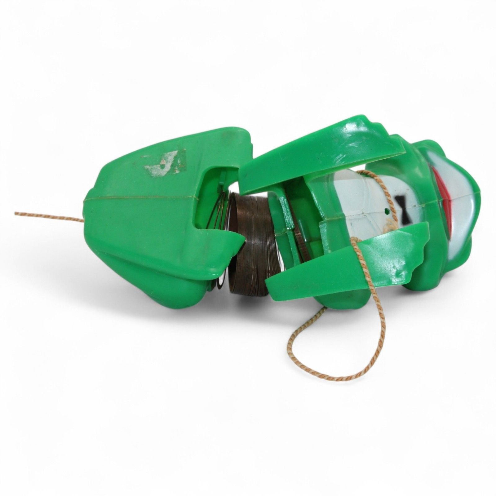 Vintage green plastic frog with pull-along rope and built-in cassette/spool tape mechanism. Frog wears a painted tuxedo bib and has a red smiling mouth. Pull the cord to wind the internal tape wheel and release it to watch the frog's "belly" spool slowly unwind, likely playing a jingling or recorded sound. Charming retro mechanical toy — a whimsical novelty from days gone by!
